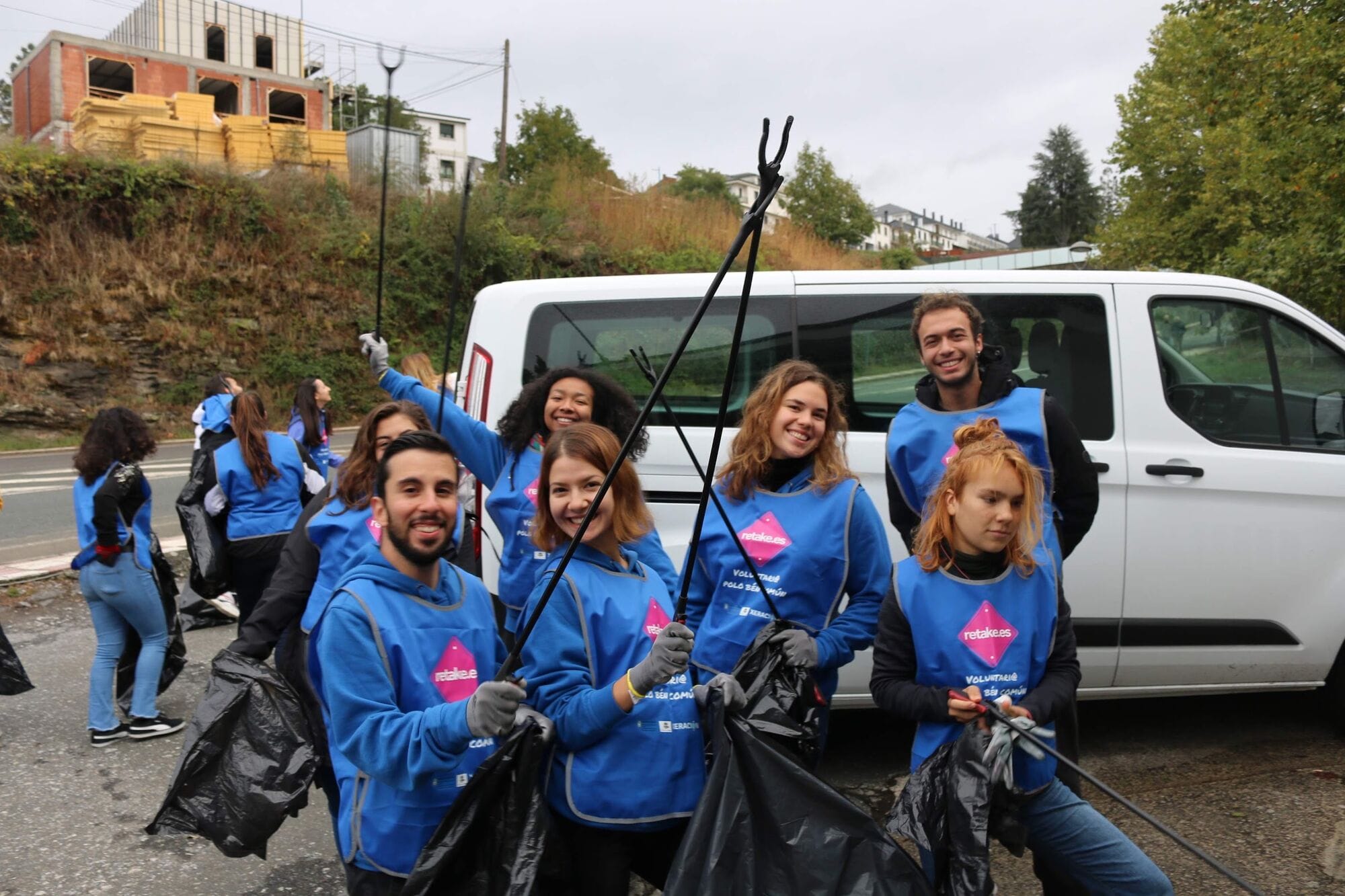 Voluntarios de Retake con chalecos azules, pinzas y bolsas, sonriendo junto a una furgoneta