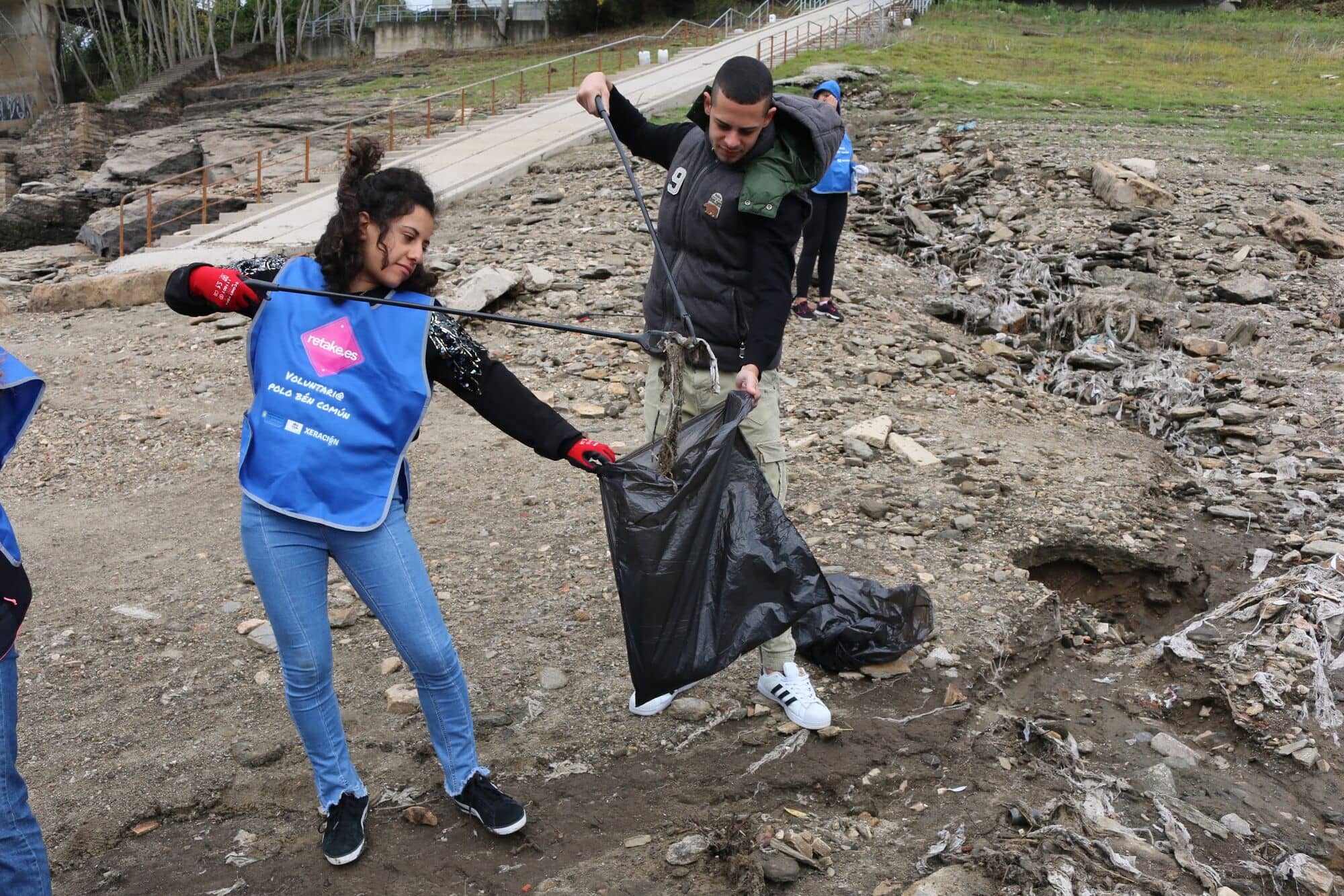 Dos voluntarias recogen basura en la orilla de un embalse
