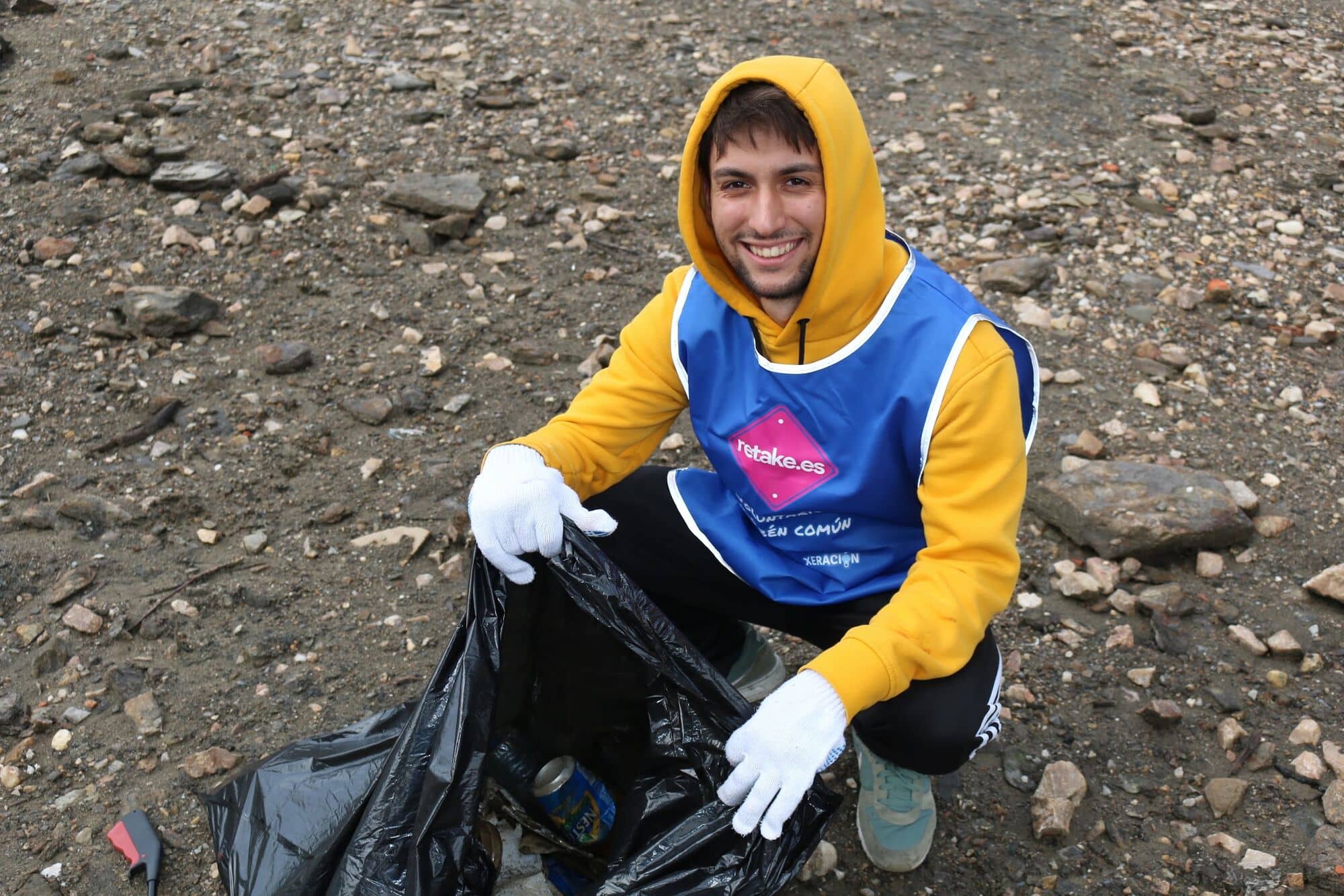 Voluntario sonriente con sudadera amarilla y bolsa de basura